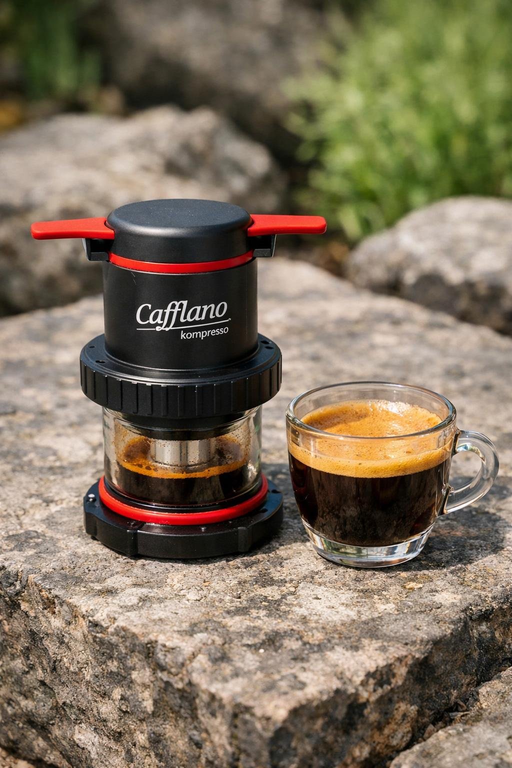 Cafflano Kompresso portable espresso maker with fresh espresso on a stone surface outdoors